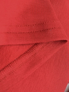 Makro-Detail der Doppel-Nadel-Saum und Overlock-Naht am roten Strickkleid Stoff