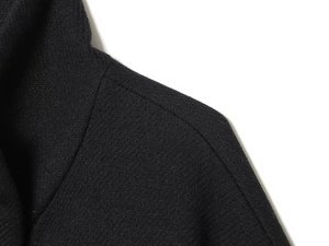 Primer plano de abrigo negro de lana con textura de sarga y detalle de costura de hombro