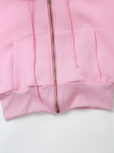 Detail view of pink hoodie showing metal zipper, side pockets, and ribbed hem with drawstrings
