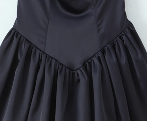 Detail of black satin dress featuring a low V-waistline and pleated voluminous skirt