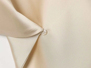 Gros plan sur la texture satinée champagne et un bouton en résine sur la robe