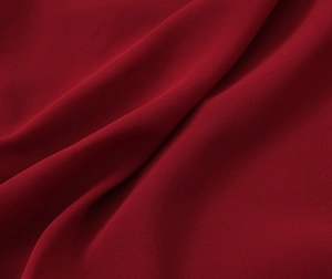Dettaglio del tessuto crepe bordeaux scuro che mostra pieghe morbide e trama granulosa
