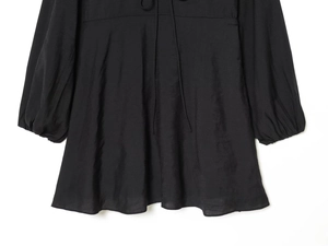 Detailweergave van zwarte jurk met V-hals, lange mouwen, getextureerde stof en trekkoord