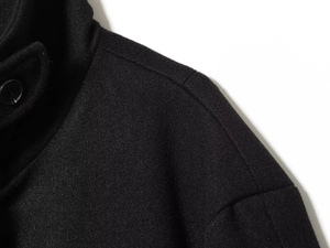 Close-up of black wool coat shoulder with smooth stitching and button detail
