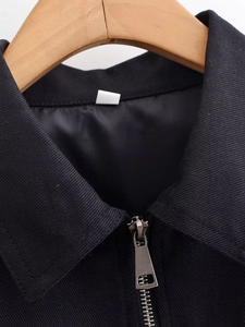 Detail shot of the metal zipper and collar on a textured black sequined jacket for women