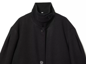 Detail of high-neck black wool coat showing pleated shoulder and large button
