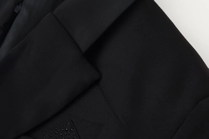Detail of a black waist-tie blazer dress featuring metallic zipper and bead embellishments