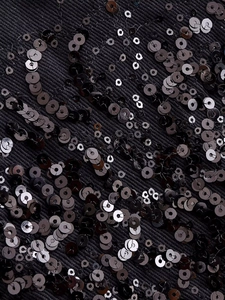 Macro detail of glossy black sequins and twill fabric texture on a fashion jacket