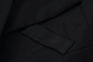 Macro detail of black blazer dress showing textured fabric and rhinestone triangle trim