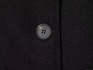Close-up of premium black coat fabric with a classic four-hole resin button detail