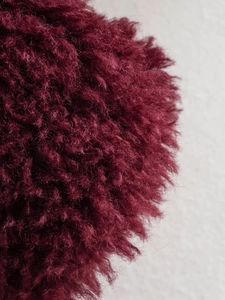 Macro shot of fluffy wine red faux fur pom-pom detail with soft fiber texture