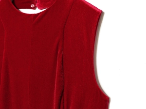 Detail of red velvet sleeveless dress showing round neckline and pink button closure