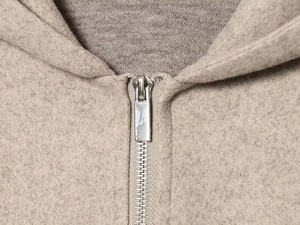 Detail shot of a neutral beige fleece jacket featuring a silver metallic zipper and soft texture