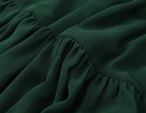 Dettaglio macro del tessuto in chiffon verde scuro con lavorazione a pieghe e increspature