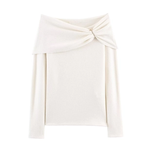 Detailed close-up of cream off-shoulder knit top with gold safety pin accent