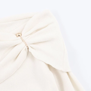 Detailed view of beige knit fabric with elegant twist design and gold sphere pin accessory