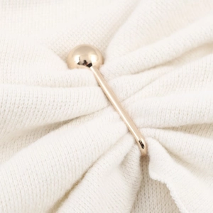 Close-up of golden metal pin with spherical end on white knit fabric texture
