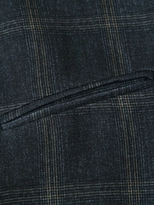 Macro detail of charcoal grey plaid fabric showing a precise welt pocket and fine stitching