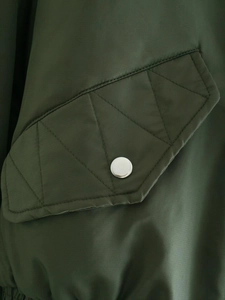 Macro d'un blouson aviateur vert olive avec rabat de poche matelassé et bouton argenté