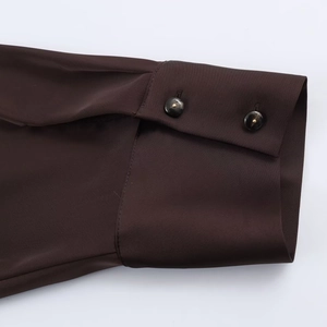 Detail of dark brown satin shirt cuff featuring elegant gold-trimmed buttons and smooth texture