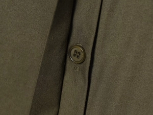 Detail of army green poplin fabric with a four-hole resin button and precise stitching