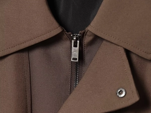 Dettaglio della giacca marrone in twill con zip in metallo e bottone a pressione