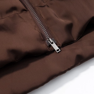 Detailed close-up of a brown quilted puffer jacket featuring a sleek metal zipper pull