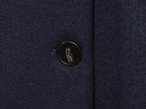 Macro shot of dark navy wool blend fabric with amber-textured button detail