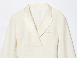 Detail of slim-fit off-white blazer dress featuring peak lapels and structured waist seams