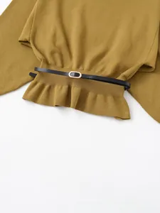 Dettaglio del top in maglia verde senape con sottile cintura nera e fibbia dorata