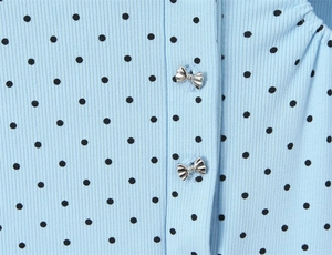 Close-up of light blue ribbed knit fabric with black polka dots and silver bow buttons