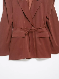 Detail eines rostbraunen Blazers mit Reverskragen, Bindegürtel und flachen Taschen