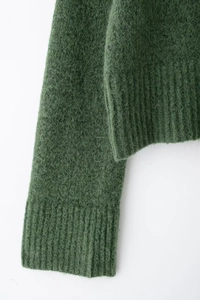 Dettaglio dei polsini e dell'orlo in maglia a coste su un maglione verde effetto mohair