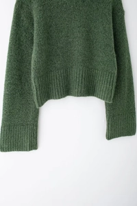Dettaglio del maglione in maglia verde scuro con texture peluche e polsini e bordo a coste