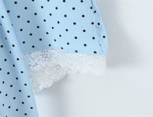 Detailed view of light blue knitted fabric with black polka dots and white lace hem trim