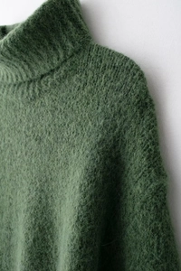 Dettaglio maglione in maglia verde scuro con collo alto e morbida texture in mohair