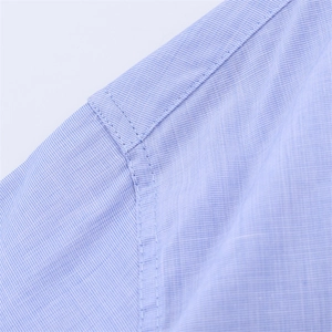 Detail of meticulous stitching on light blue shirt shoulder seam with fine texture