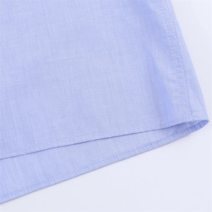 Detailed close-up of double-stitched hem on light blue textured shirt fabric