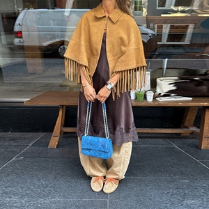 Detail shot of camel suede poncho with long fringe hem and blue luxury chain bag
