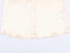 Detailed close-up of light beige silk shirt featuring clear buttons and curved hem stitching