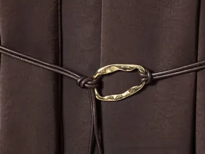 Detailed close-up of a golden wavy metal buckle on a dark brown satin dress waist