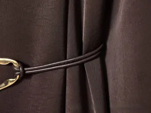 Close-up of a satin dress waist belt with a distinctive gold irregular metal buckle