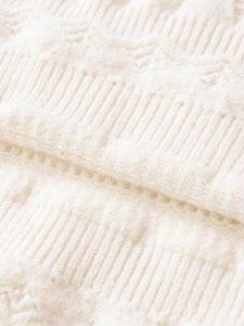 Detailed close-up of white knit fabric showing cable stitch patterns and ribbed texture