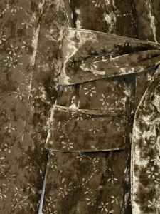 Macro detail of olive green velvet suit showing floral print and waist belt texture