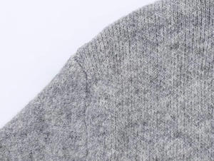 Macro shot of soft grey knit sweater showing high-quality stitching and wool texture