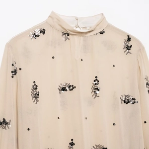 Detail of high-neck beige chiffon blouse featuring black and silver sequin flower patterns