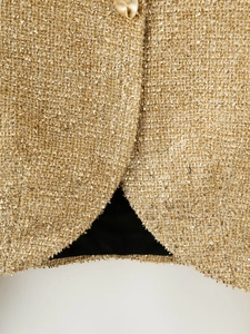 Detail of gold metallic tweed fabric with shiny texture and decorative embossed button