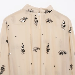 Close-up of semi-sheer beige blouse with intricate black and silver sequin flower embroidery