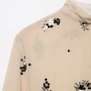 Close-up of champagne sheer shirt featuring intricate black and silver sequin embroidery
