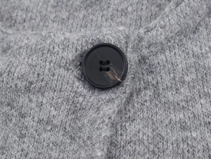 Detail shot of a black four-hole resin button on a gray chunky knit sweater cardigan